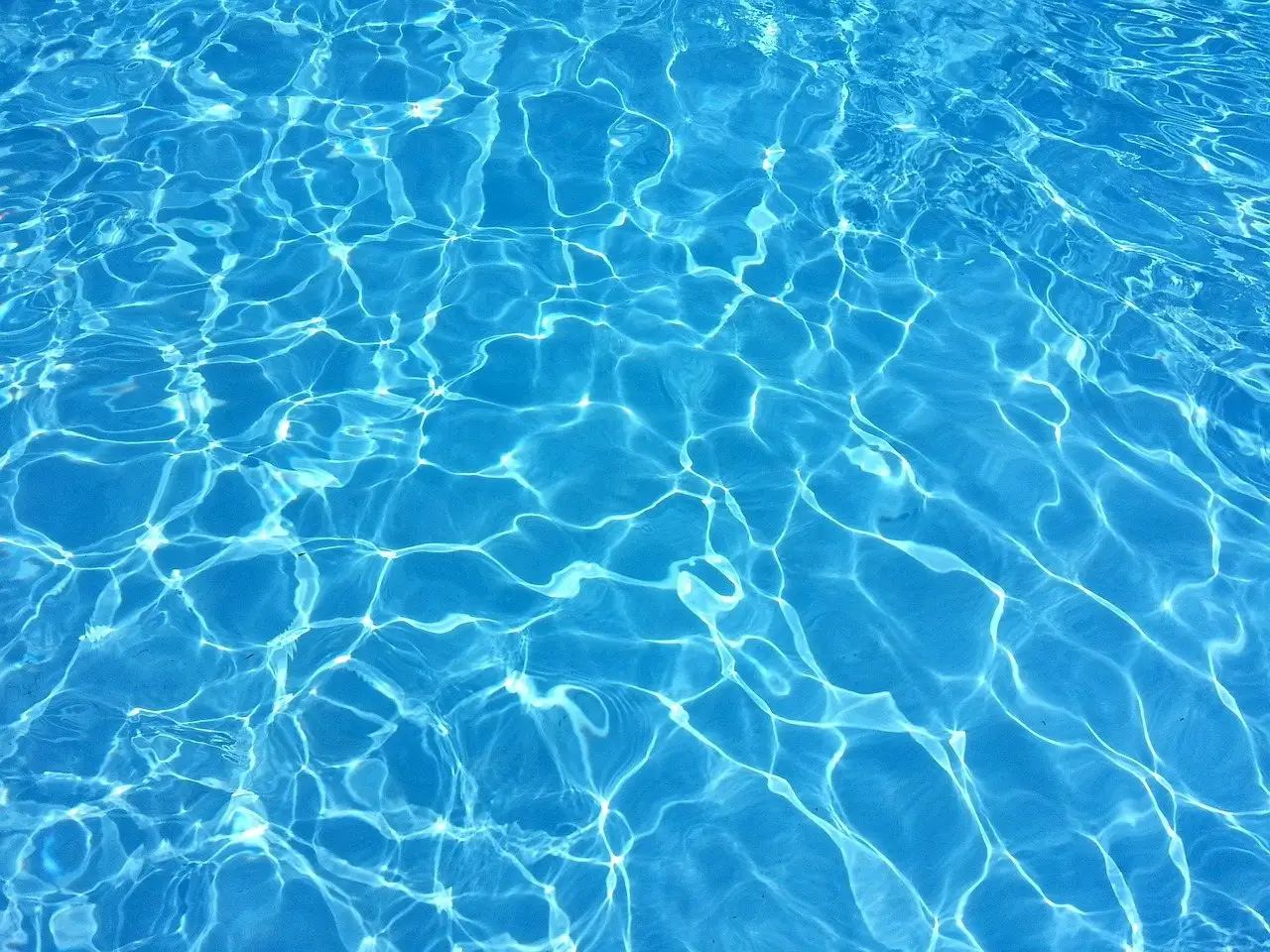 Clear blue swimming pool water with sunlight rippling across the bottom