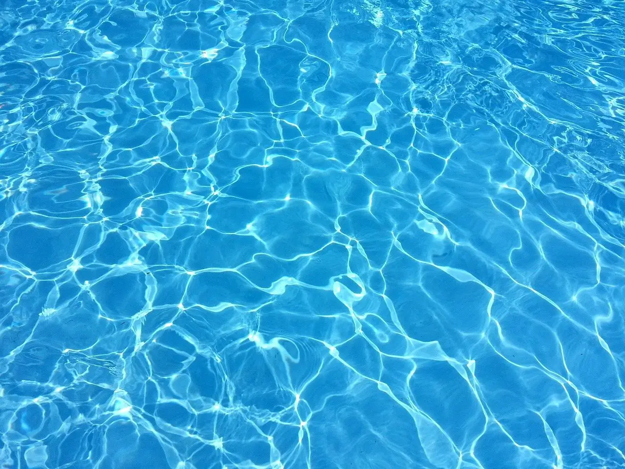 Clear blue swimming pool water with sunlight rippling across the bottom