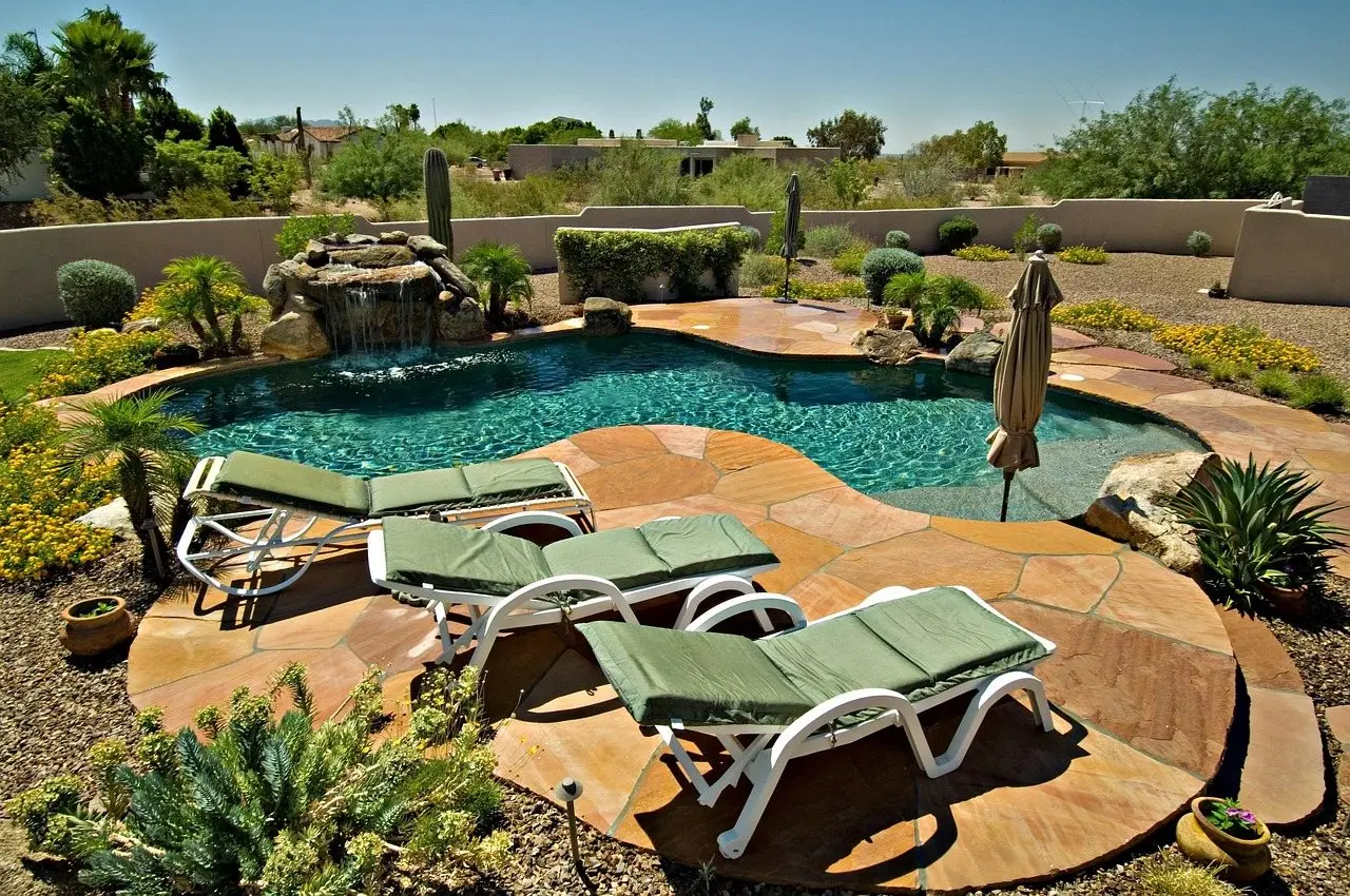 A small curved backyard pool with a flagstone surround and two loungers