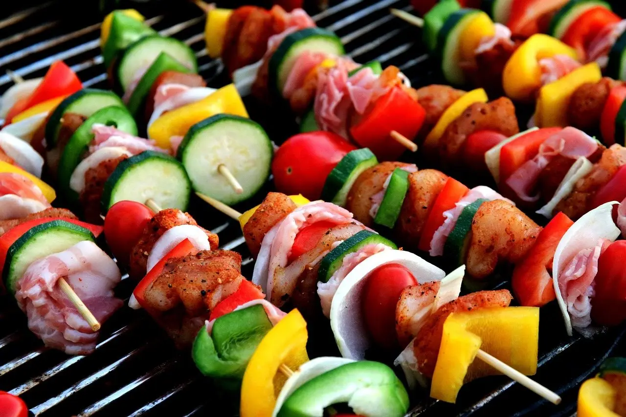 Meat and vegetable skewers cooking on the bars of a grill