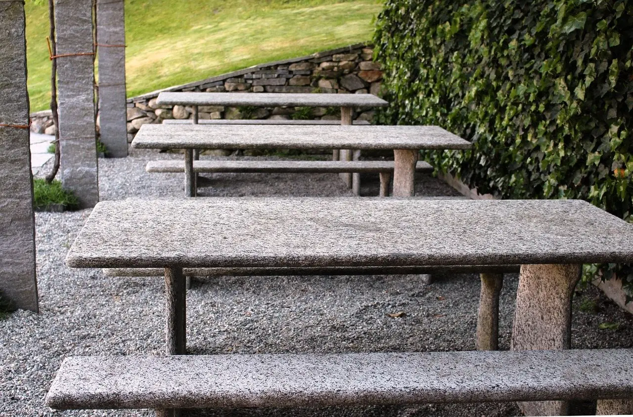 Stone tables and benches set out on a raked gravel surface beside a dry stone wall
