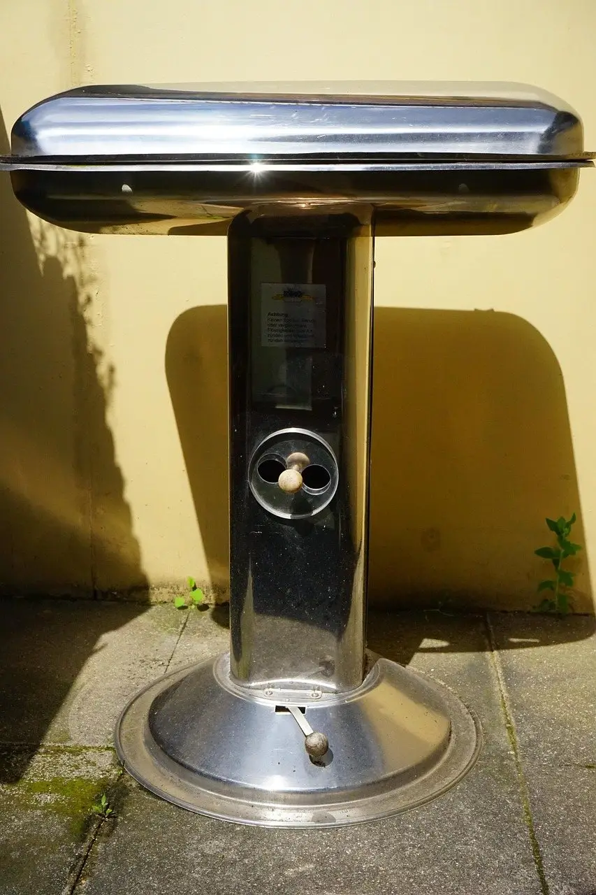 A closed stainless steel barbecue standing on paving against a plain rendered wall