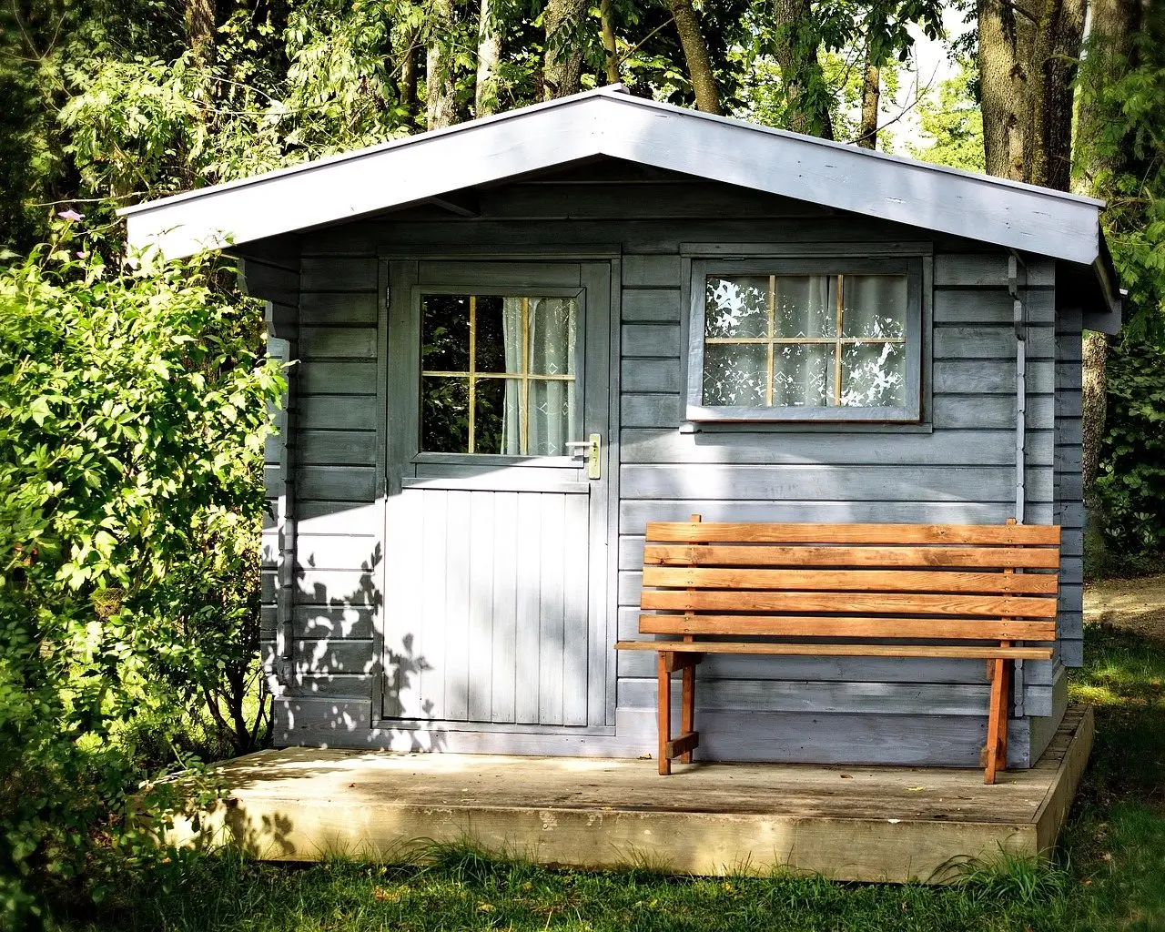 A grey painted timber garden shed with a bench against it, surrounded by shrubs