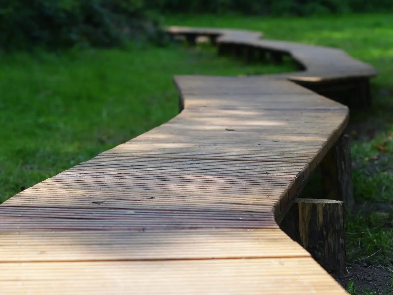 A zig-zag boardwalk of grooved decking boards running across grass under dappled light