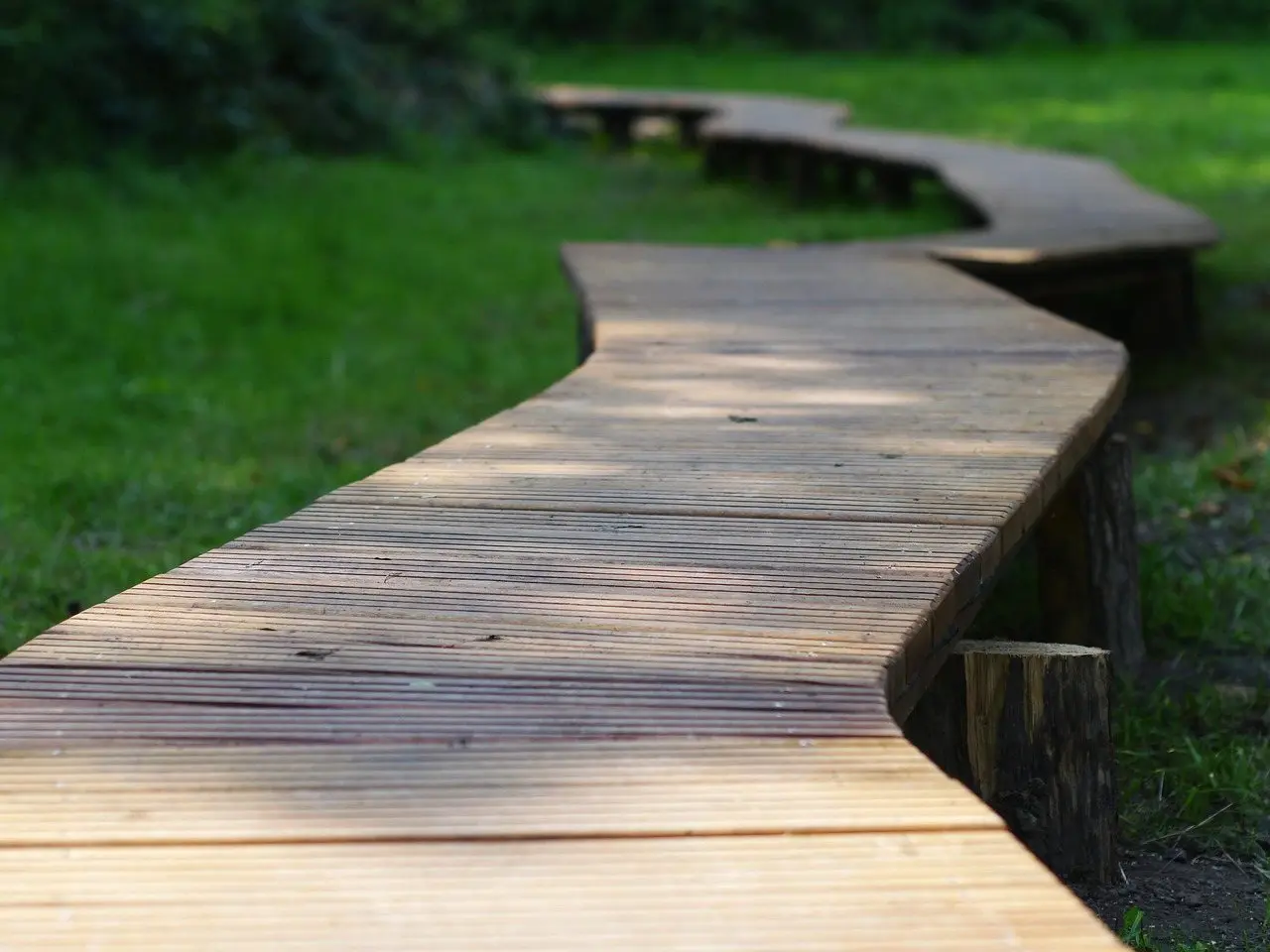 A zig-zag boardwalk of grooved decking boards running across grass under dappled light