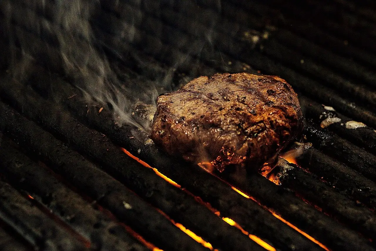 A steak searing on grill bars with flames visible through the grate beneath