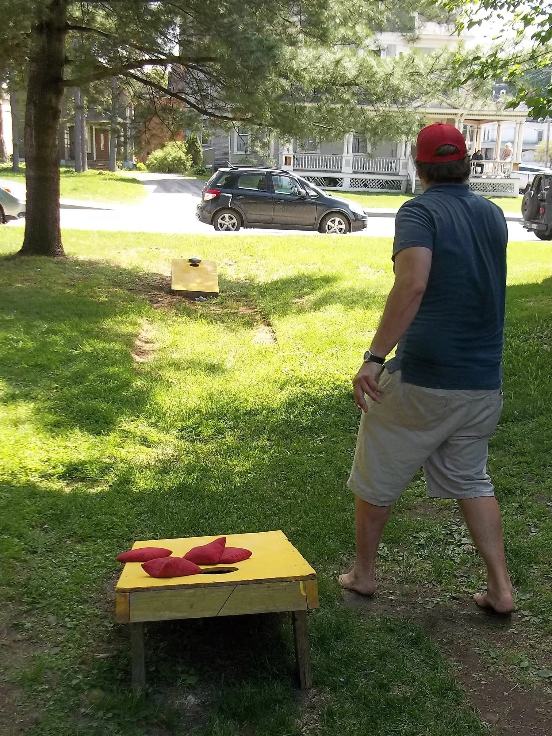 Someone throwing a bean bag at a cornhole board on a lawn